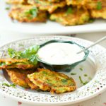 A plate of golden baked zucchini fritters garnished with fresh herbs and served with a side of spicy aioli dip.