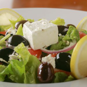A plate of Greek Salad with feta cheese and olives, topped with a lemon wedge.