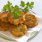 A plate of golden-brown potato fritters, garnished with fresh herbs, sitting atop a white tablecloth.