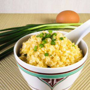 A golden-brown bowl of egg fried rice with a spoon and a few scallions on the side.
