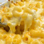 Close-up of a baking dish of mac and cheese topped with melted cheese, with a few scoops removed to show the creamy inside