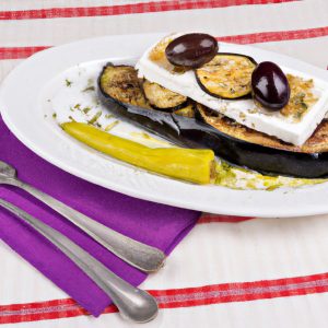 Image of a grilled eggplant with feta cheese and olives on a white plate with a colorful napkin
