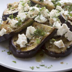 A plate of grilled eggplant slices topped with feta cheese, olives and herbs.