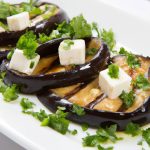 A photo of a plate of grilled eggplant with feta and olives, garnished with chopped parsley