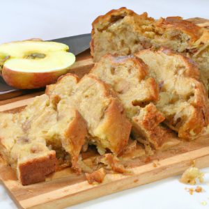 A golden brown apple fritter bread cut into slices, with a few un-sliced pieces left on the cutting board.