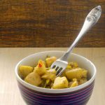 A bowl of Indian-spiced potato salad with a fork and a spoon in the background.