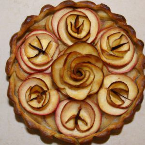 A golden-brown tart with four rose-shaped apples arranged in the center.