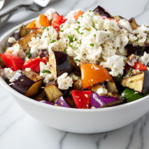 A bowl of grilled eggplant salad with a variety of colorful vegetables, topped with feta cheese.