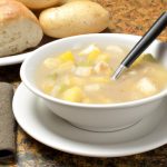 A steaming bowl of Italian Potato Soup with a spoon and a slice of crusty bread on the side.