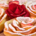 A golden, flaky crust filled with sweet apples and topped with rose-shaped slices of apple, sprinkled with powdered sugar.