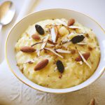 A bowl of creamy, golden Indian Rice Pudding, topped with sliced almonds, raisins and a sprinkle of cardamom.