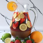 A large pitcher of Japanese sake sangria surrounded by limes, oranges and strawberries.