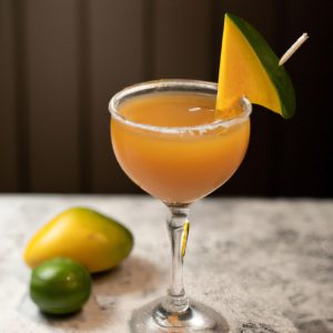 A glass of Indian spiced mango margarita with a slice of mango and a lime wedge on the side