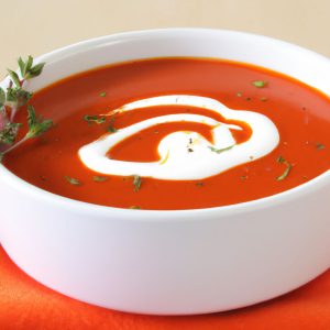 A bowl of roasted tomato soup with a swirl of cream and herbs on top.