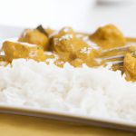 A close-up of a plate of Indian chicken curry with a spoon and a side of basmati rice.
