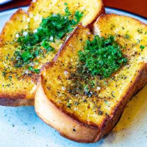 A plate of golden-brown, toasty garlic bread with herbs sprinkled on top