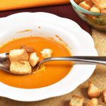 A bowl of hearty roasted butternut squash soup with a spoon in it and a few croutons sprinkled on top.