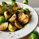 A plate of roasted brussels sprouts and apples with a sprinkling of fresh herbs