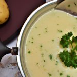 A pot of creamy potato soup with a spoonful of potatoes and a sprinkle of parsley on top.