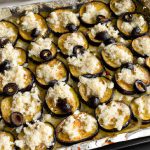 A close-up of a baking sheet filled with baked eggplant slices topped with feta cheese and olives