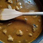 Prompt for an AI image generator: A pot of Indian chicken curry with a wooden spoon in the center.