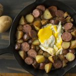 An overhead shot of a cast iron skillet filled with potatoes, sausage, and eggs.