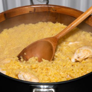 A large pot of golden yellow chicken and rice steaming with a wooden spoon resting on the edge