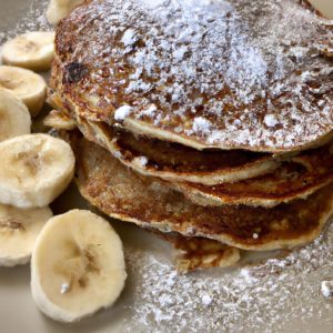 A plate of fluffy banana oat pancakes topped with fresh banana slices and a sprinkle of powdered sugar.