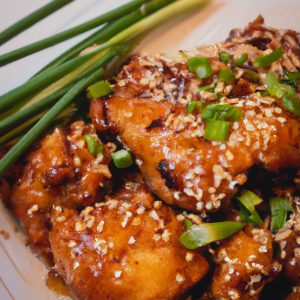 A plate of golden-brown Chinese sesame chicken, the sesame seeds and green onions adding a pop of color.