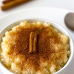 A bowl of creamy, golden-brown coconut rice pudding with a drizzle of honey and a sprinkle of cinnamon on top.