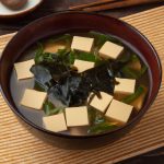 A bowl of miso soup with silken tofu, bamboo shoots, and wakame seaweed.