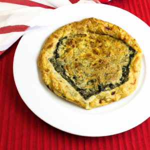 A delicious, golden-brown French Spinach Galette on a white plate with a red napkin on the side.