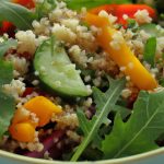 Close-up image of a bowl of Herbed Quinoa and Arugula Salad with colorful vegetables and herbs sprinkled on top.