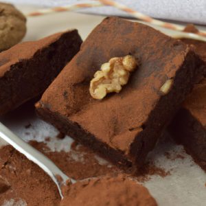A close up of a classic Italian chocolate brownie with walnuts and a sprinkle of cocoa powder.