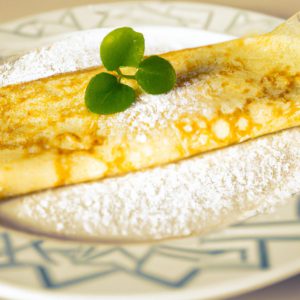 A golden crepe sitting on a classic white plate, with a sprig of herbs and a sprinkle of confectioner's sugar.