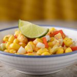 Close-up of a bowl of Mexican Street Corn Salad with a fresh lime wedge on the side