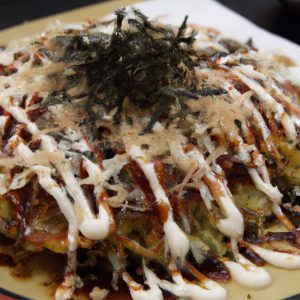A plate of freshly made Japanese okonomiyaki pancakes, sprinkled with bonito flakes, with a side of mayo and soy sauce.