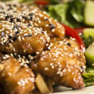 Close-up of a plate of Chinese sesame chicken with a side of vegetables.
