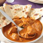 A steaming bowl of Slow Cooker Chicken Tikka Masala with a spoon in the center, served with a side of naan bread.