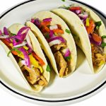 Image of colorful Mexican tacos with chicken, peppers, and onions on a plate against a white background.