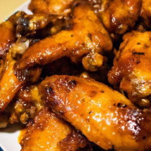 A plate of savory BBQ chicken wings fresh from the oven. The wings are a golden brown color and the sauce is glistening in the light.