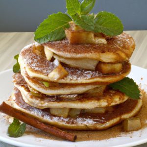 A stack of three Apple Pie Pancakes topped with a generous sprinkle of cinnamon, a dollop of maple syrup, and a sprig of fresh mint.