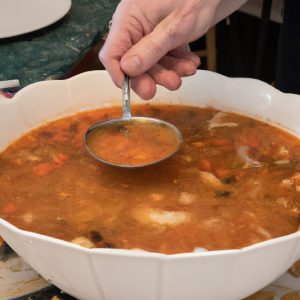 A large bowl of Mediterranean soup with a spoon next to it, with a hand reaching in to take a spoonful from the bowl.