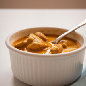 A bowl of slow cooker Indian chicken curry with a spoon, sitting on a white table.