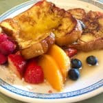 A plate of French Toast with syrup and a side of fresh fruit.