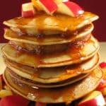 A stack of three delicious-looking, golden-brown pancakes topped with fresh apples and a drizzle of syrup.