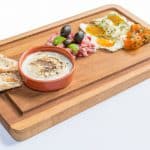A warm, savory dish of Mediterranean breakfast appetizers served on a rustic wooden platter.