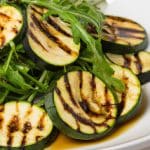 A grilled zucchini and arugula salad with a tangy balsamic vinaigrette dressing served on a white plate.