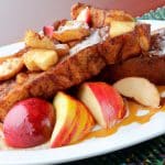 A plate of delicious apple cinnamon French toast garnished with fresh fruit and drizzled with syrup.